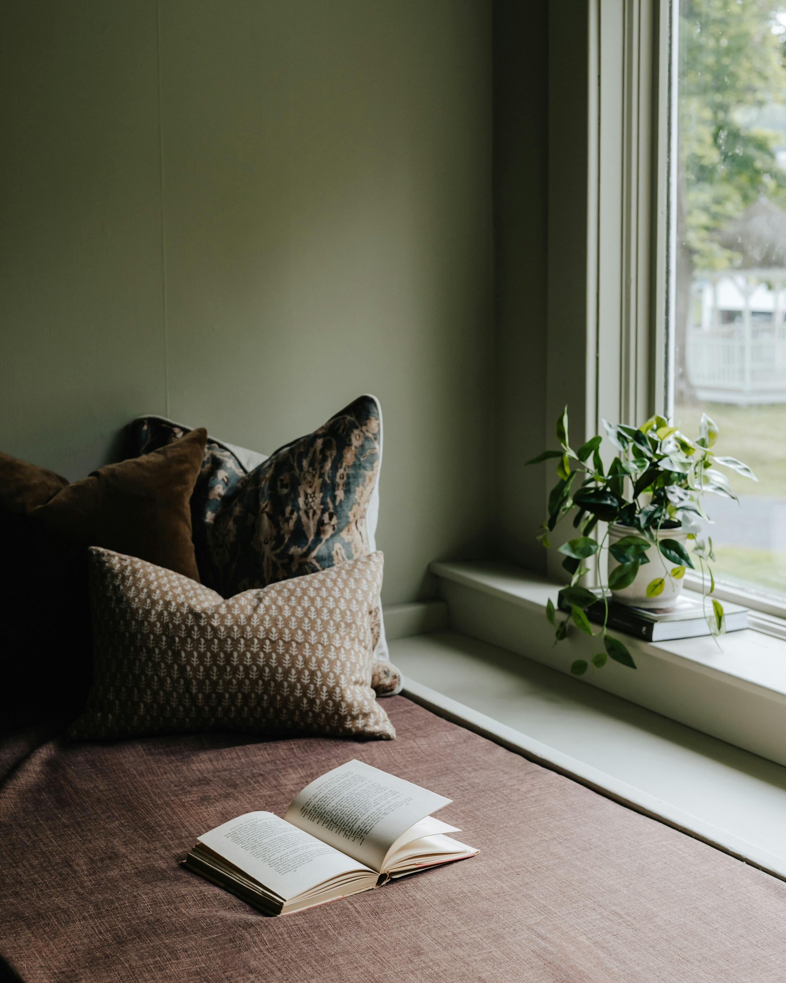 A warm, sunlit reading nook with a velvet armchair, stacked books, and warm afternoon light